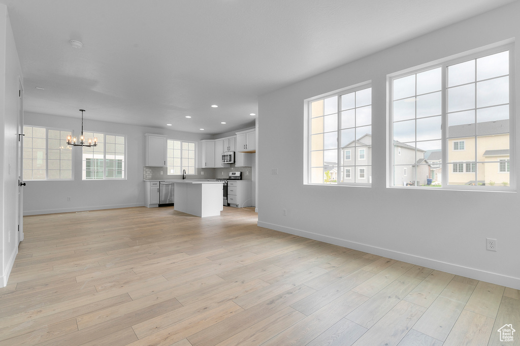 Unfurnished living room with a chandelier, baseboards, light wood finished floors, recessed lighting, and a sink