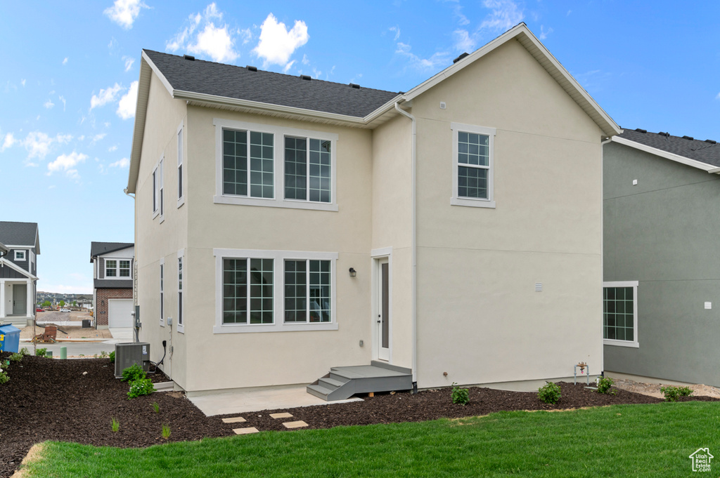 Rear view of house featuring stucco siding, a lawn, and central AC