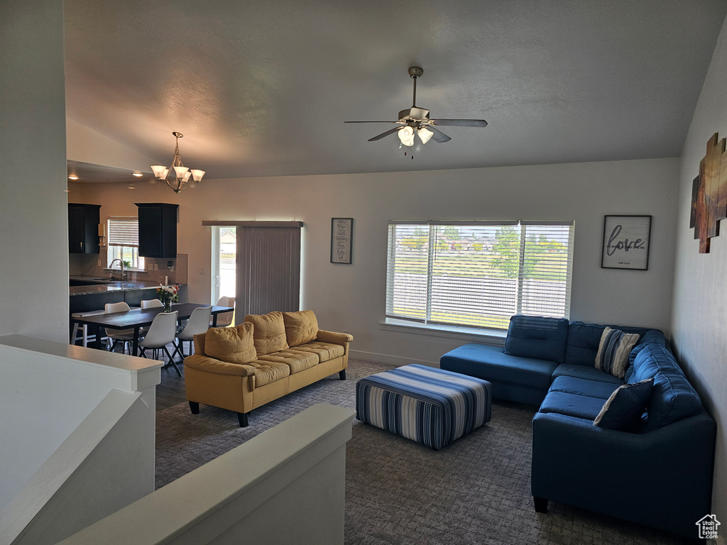 Living room with lofted ceiling, dark carpet, ceiling fan, a chandelier, and baseboards