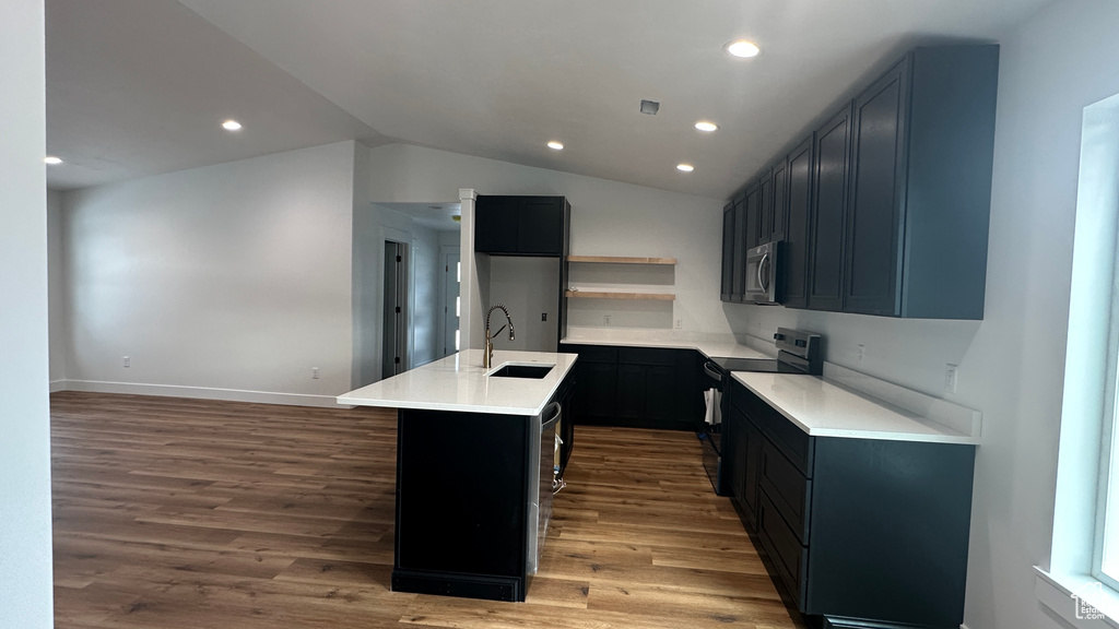 Kitchen featuring dark hardwood / wood-style flooring, sink, range with electric cooktop, vaulted ceiling, and a center island with sink