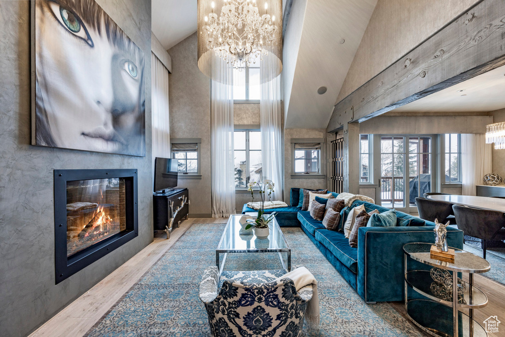 Living area with a chandelier, wood finished floors, a glass covered fireplace, and a high ceiling
