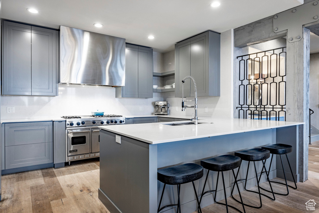 Kitchen featuring double oven range, range hood, light wood-type flooring, a peninsula, and recessed lighting