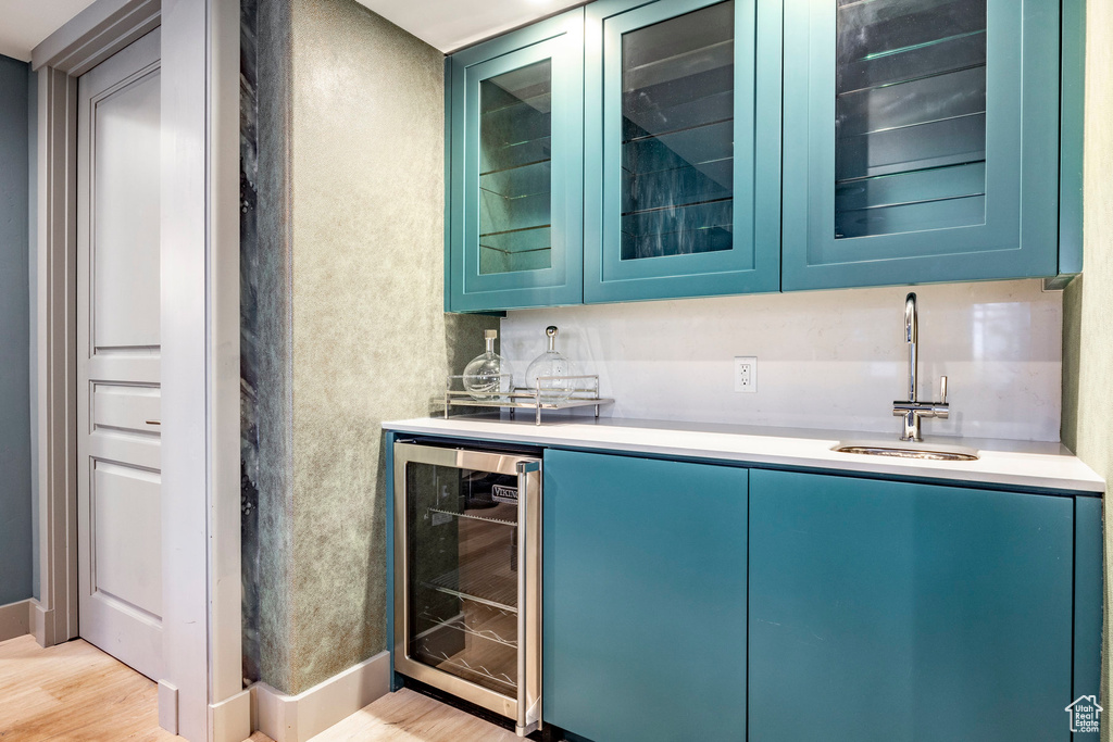 Indoor wet bar with beverage cooler, light wood-type flooring, and baseboards