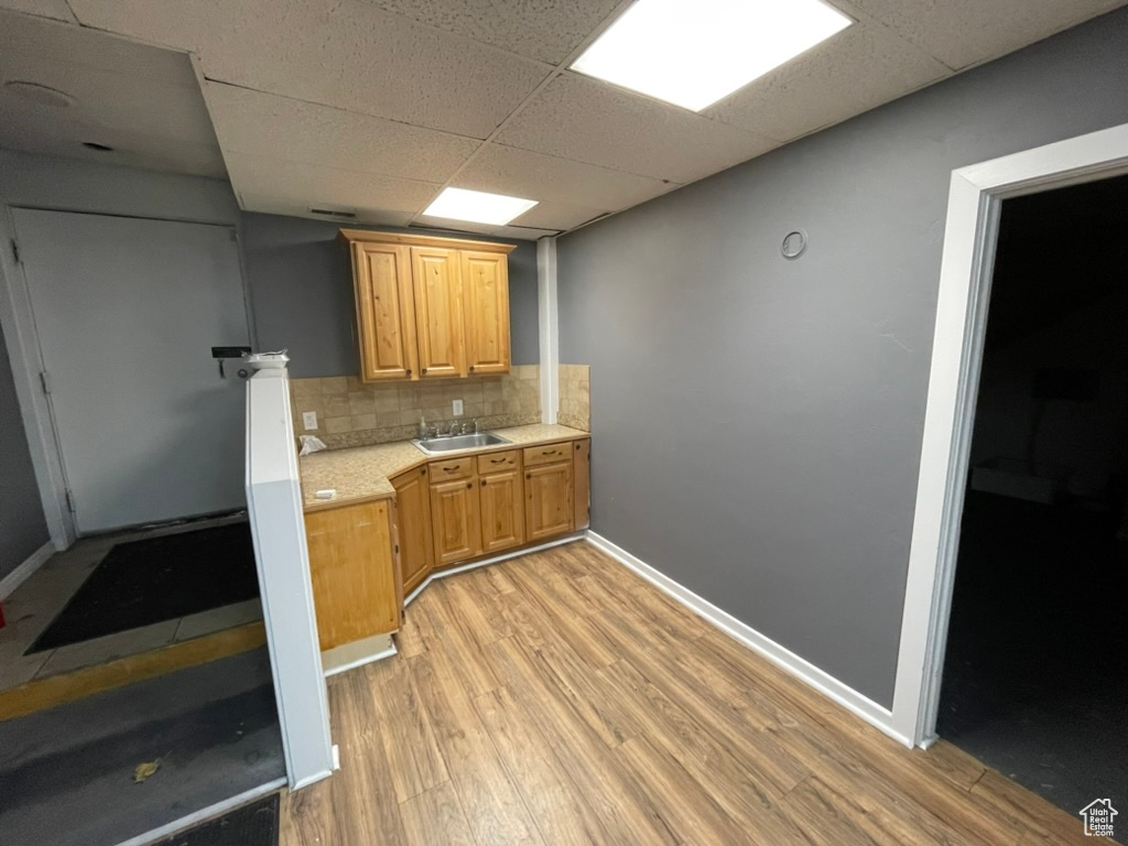 Kitchen with light wood-type flooring, backsplash, a paneled ceiling, and sink