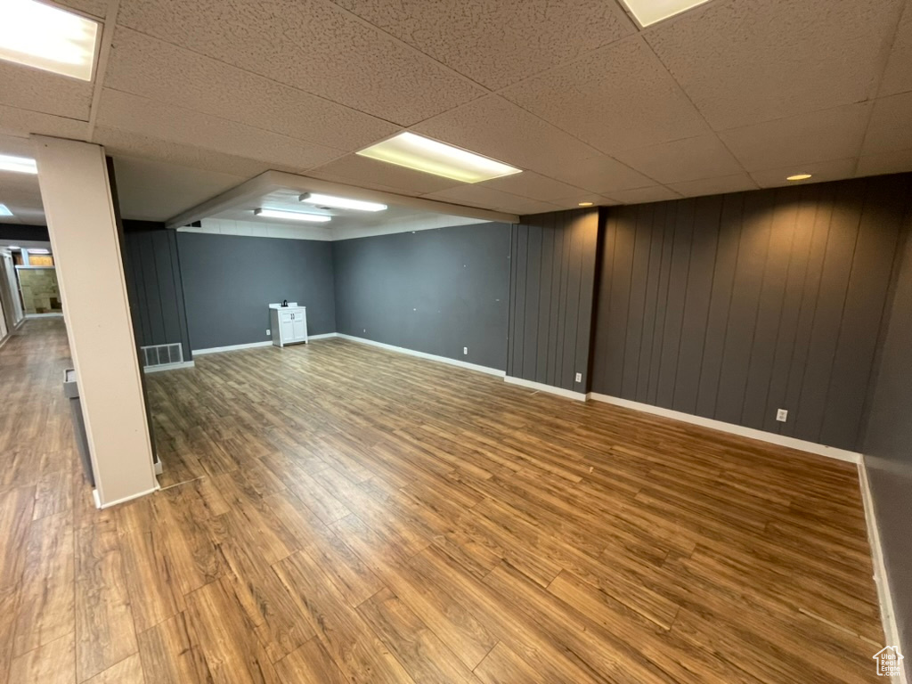 Basement with wooden walls, hardwood / wood-style floors, and a drop ceiling