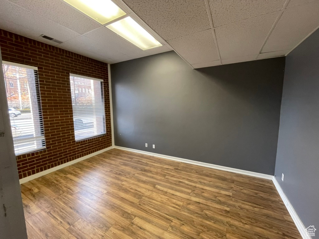 Unfurnished room featuring hardwood / wood-style floors, a drop ceiling, and brick wall