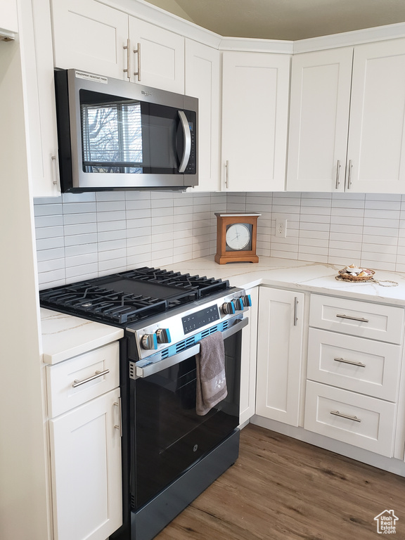 Kitchen with appliances with stainless steel finishes, dark hardwood / wood-style flooring, tasteful backsplash, and white cabinetry