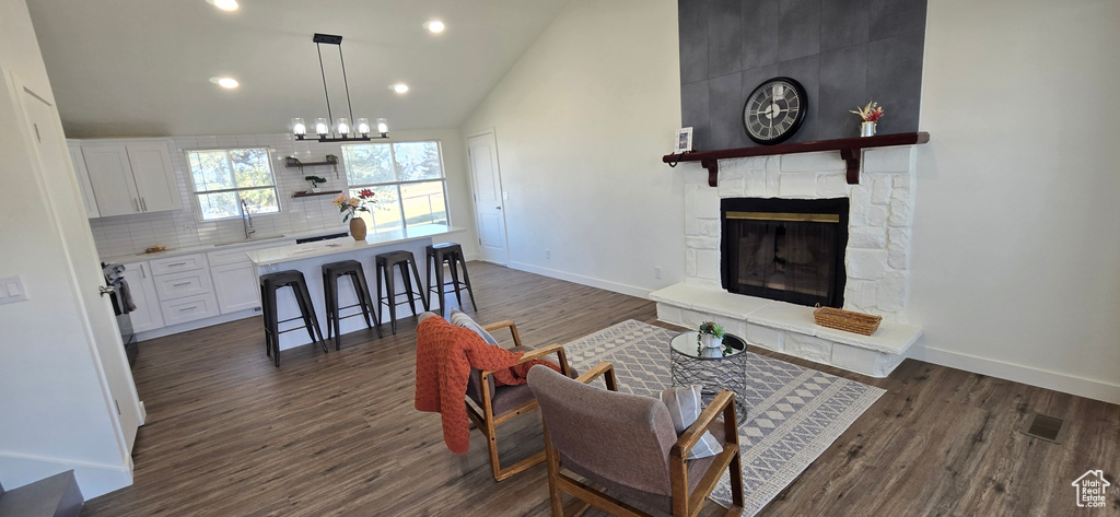 Living room with dark wood-type flooring, sink, a stone fireplace, and vaulted ceiling