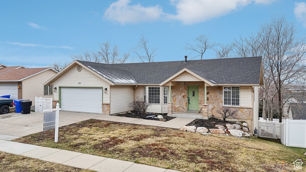 Ranch-style home with concrete driveway, an attached garage, a gate, fence, and stone siding