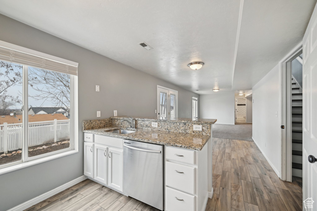 Kitchen featuring white cabinets, dishwasher, a peninsula, light wood-style floors, and a sink