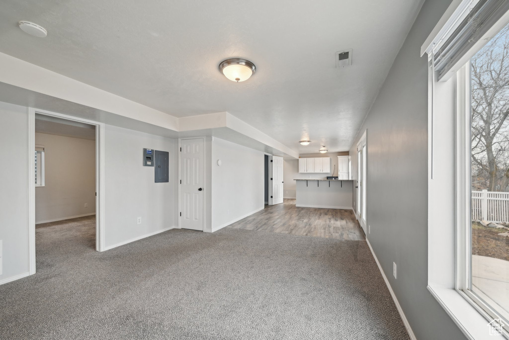 Unfurnished living room with carpet, electric panel, and baseboards