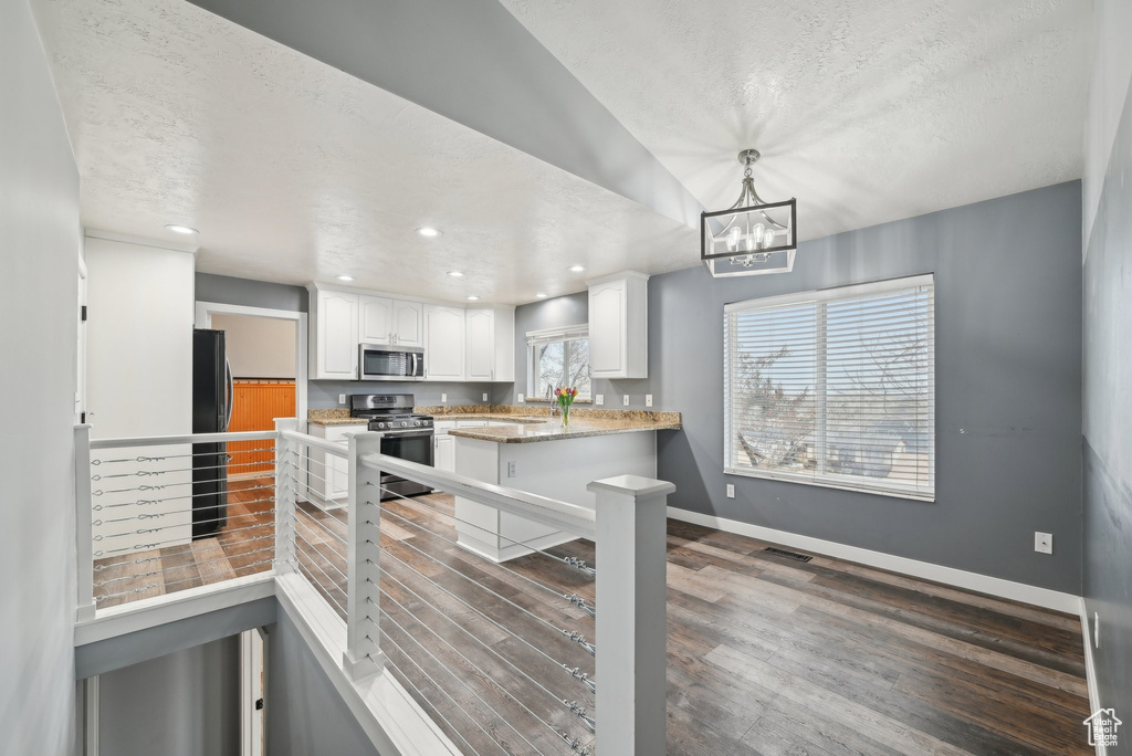 Kitchen featuring baseboards, white cabinets, wood finished floors, a peninsula, and stainless steel appliances