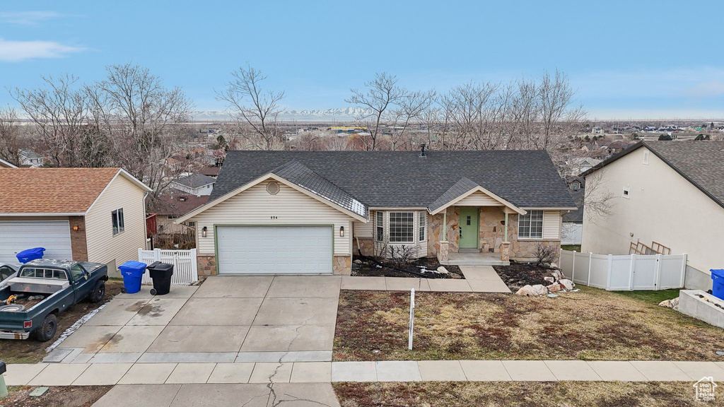 View of front of house with driveway, a garage, stone siding, roof with shingles, and fence