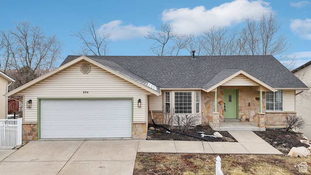 View of front of home featuring a garage, stone siding, roof with shingles, and driveway