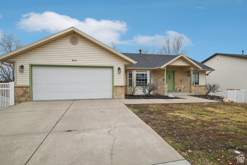 Ranch-style home featuring stone siding, concrete driveway, an attached garage, and fence