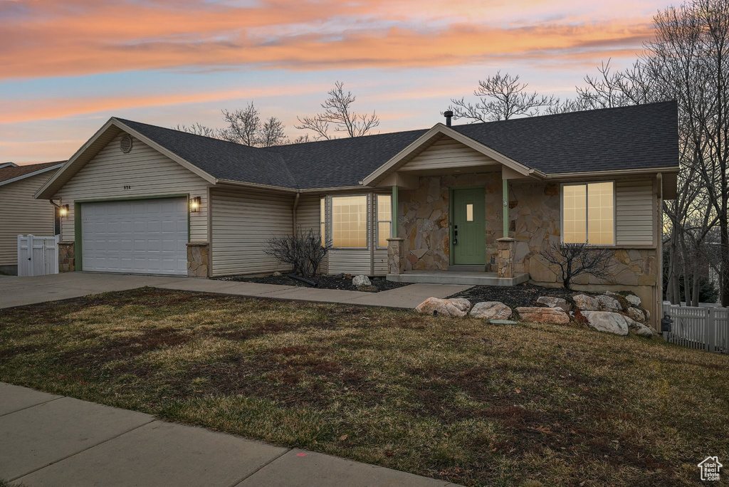 Ranch-style home featuring driveway, a shingled roof, stone siding, an attached garage, and a front yard