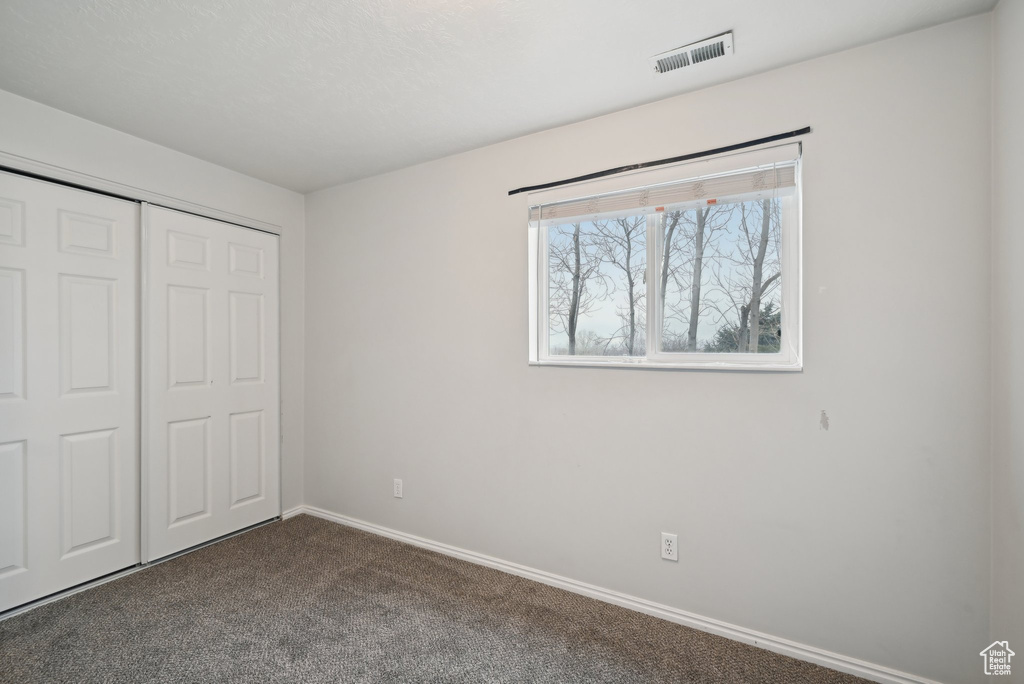 Unfurnished bedroom with dark colored carpet, a closet, visible vents, and baseboards