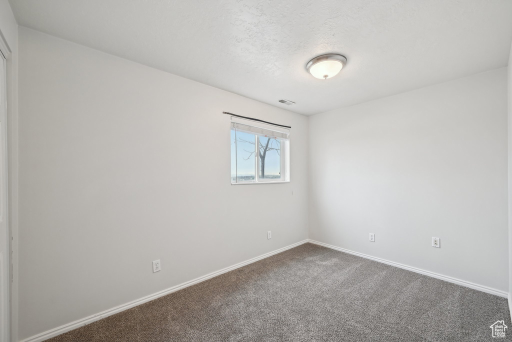 Carpeted empty room with visible vents, a textured ceiling, and baseboards