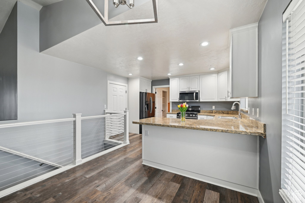 Kitchen with stainless steel appliances, a peninsula, a sink, white cabinets, and dark wood finished floors