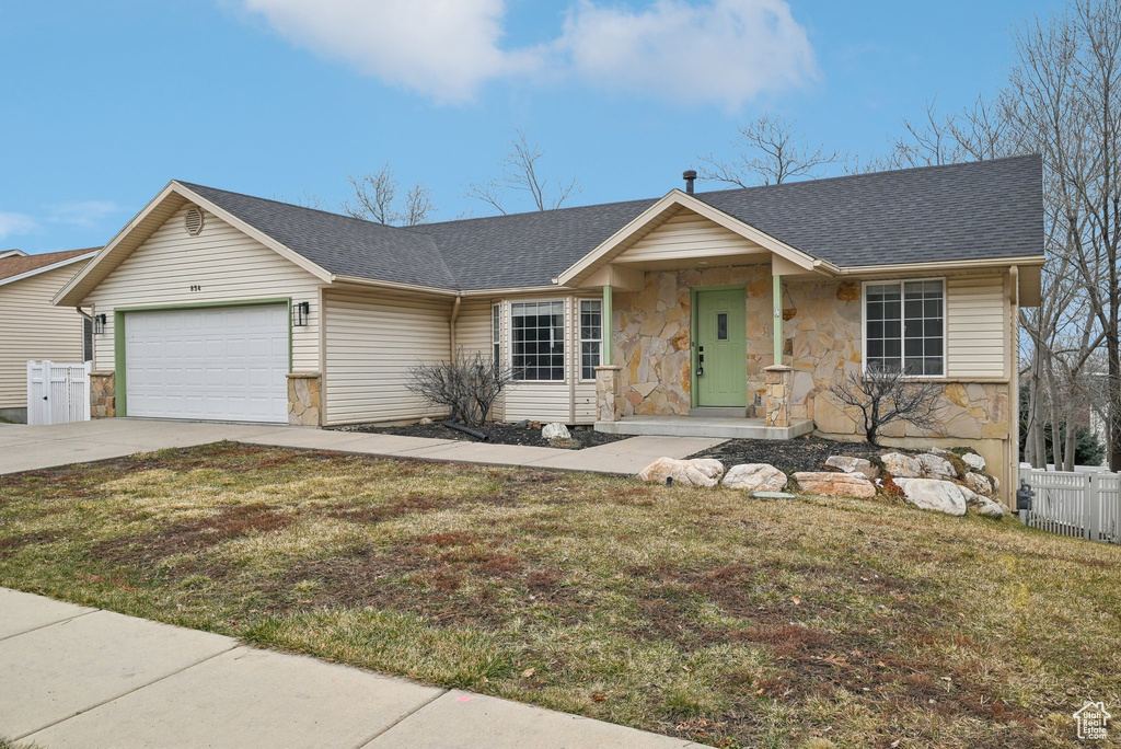 Ranch-style home with an attached garage, fence, stone siding, driveway, and a front lawn