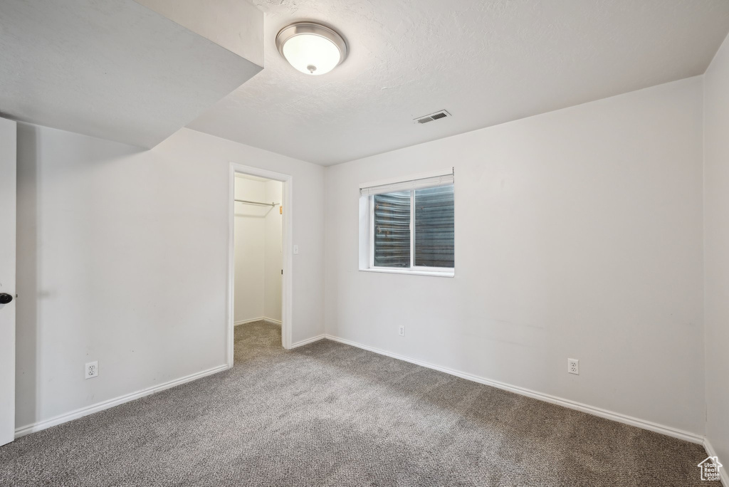 Spare room featuring a textured ceiling, carpet flooring, visible vents, and baseboards