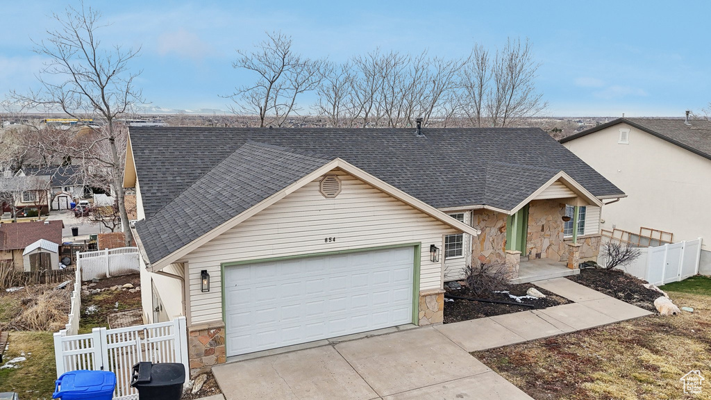 View of front of home with stone siding, roof with shingles, fence, and driveway