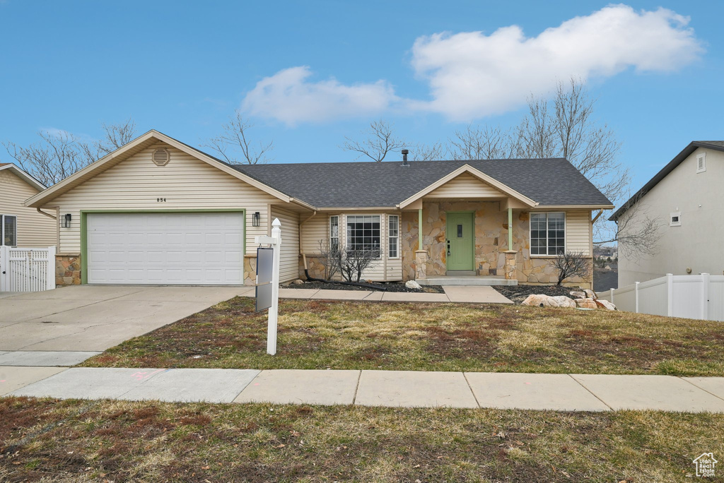 View of front of house featuring roof with shingles, concrete driveway, an attached garage, fence, and stone siding