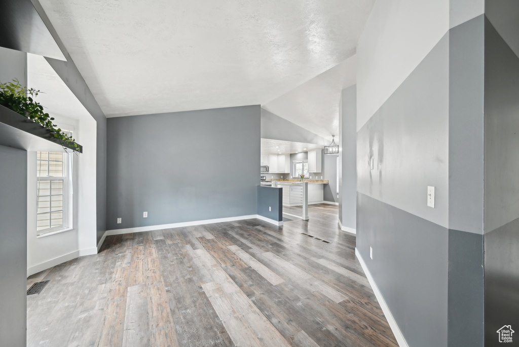 Unfurnished living room featuring lofted ceiling, wood finished floors, and baseboards