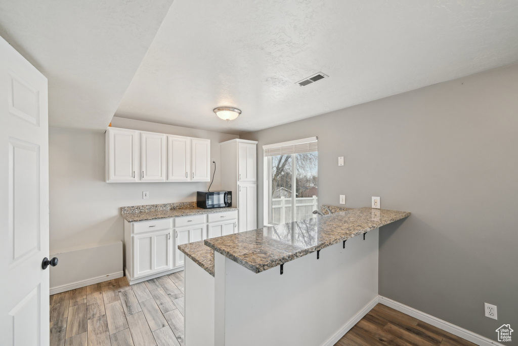 Kitchen with black microwave, a peninsula, visible vents, light wood-type flooring, and light stone countertops