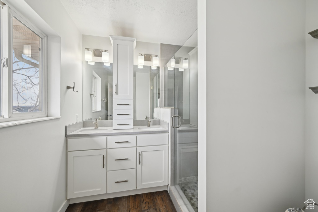 Full bathroom with double vanity, a sink, a shower stall, wood finished floors, and baseboards