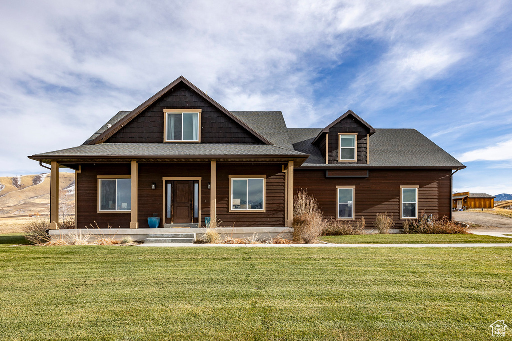View of front facade featuring a front lawn, covered porch, and roof with shingles
