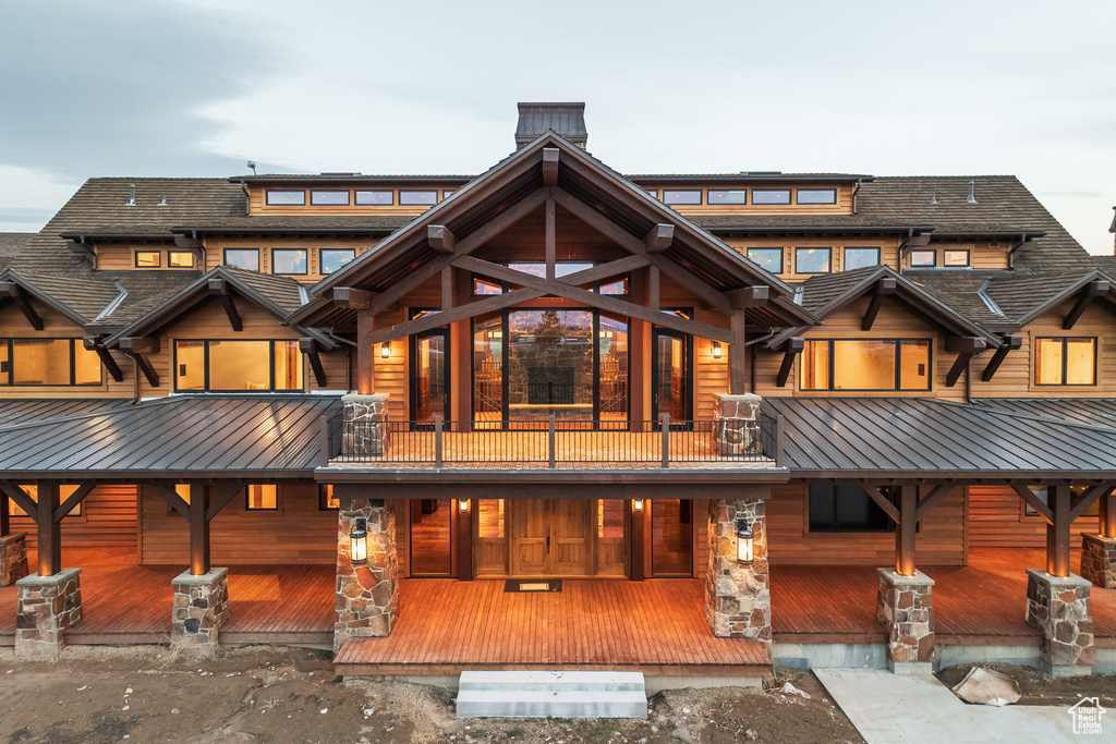 Rear view of house featuring a balcony, a chimney, a metal roof, and stone siding