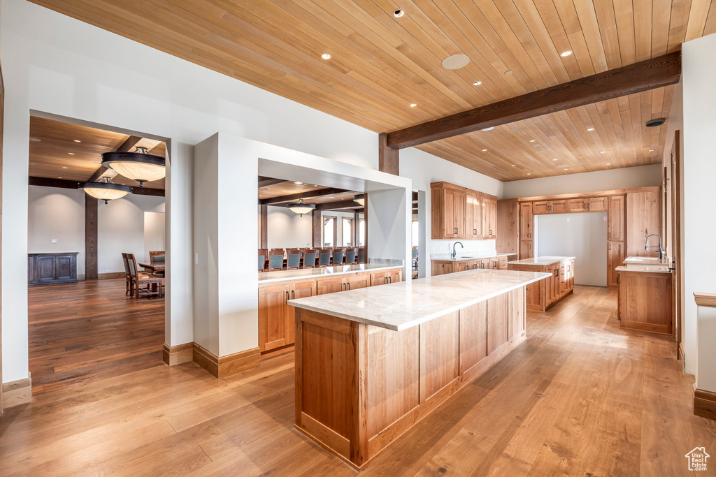 Kitchen with a large island, a wooden ceiling with exposed beams, light wood-type flooring, recessed lighting, and brown cabinets