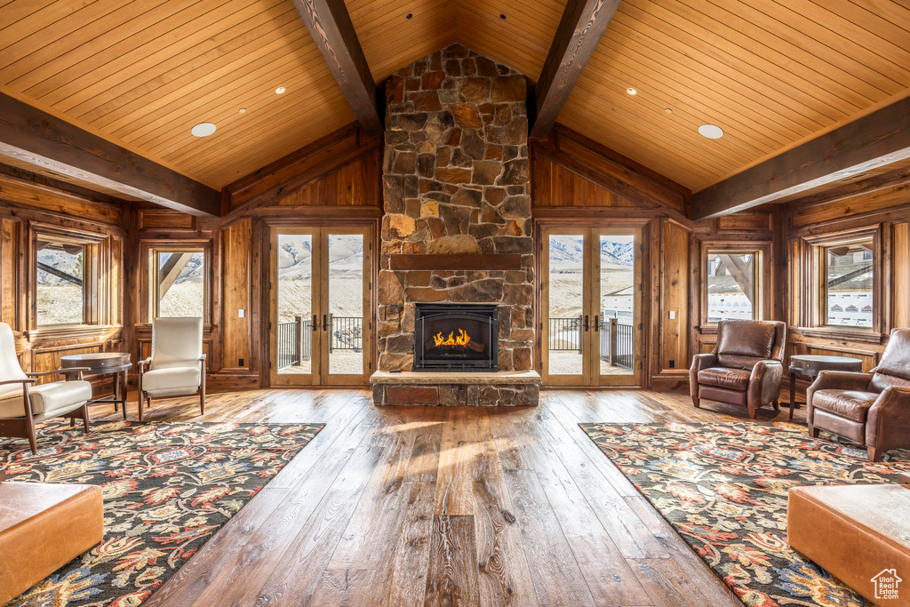 Living room with french doors, hardwood / wood-style flooring, a wooden ceiling with exposed beams, wood walls, and plenty of natural light