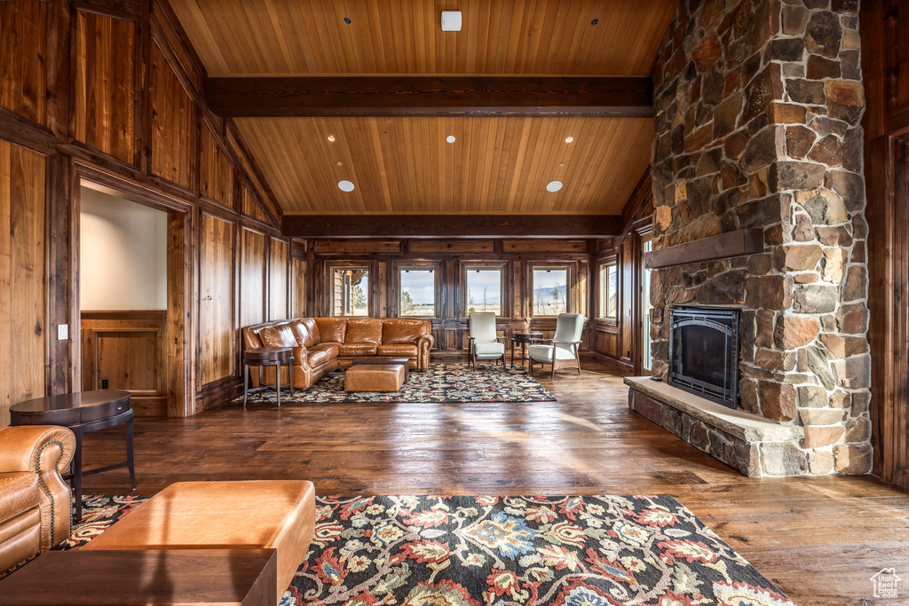 Living room featuring wood-type flooring, a wooden ceiling with exposed beams, wooden walls, a stone fireplace, and high vaulted ceiling