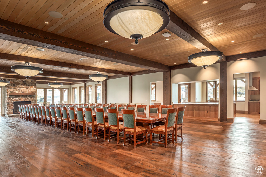 Dining space with hardwood / wood-style flooring, plenty of natural light, recessed lighting, a wood ceiling with exposed beams, and a stone fireplace