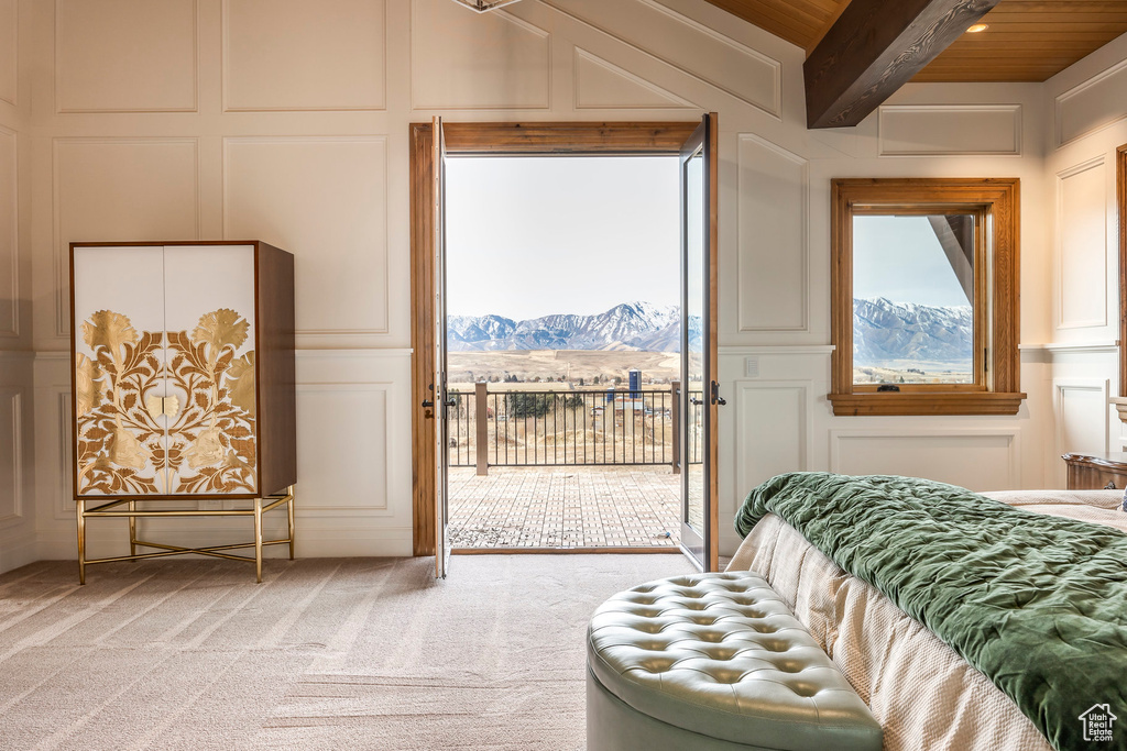 Bedroom featuring a decorative wall, a mountain view, access to exterior, light colored carpet, and beam ceiling