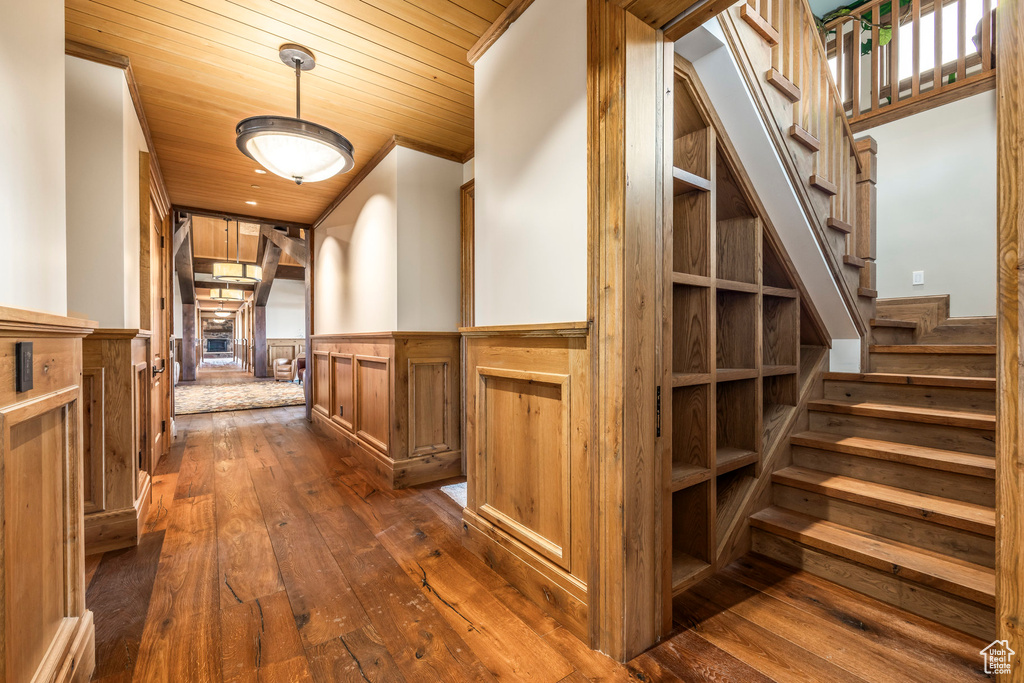 Corridor with dark wood-type flooring, a wainscoted wall, wood ceiling, and stairway