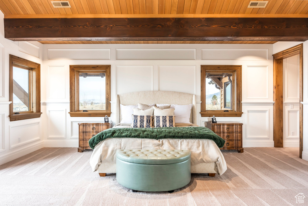 Bedroom with a decorative wall, a wooden ceiling with exposed beams, light carpet, and multiple windows