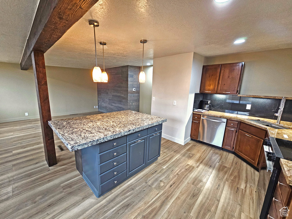 Kitchen with sink, dishwasher, hanging light fixtures, a center island, and light stone counters