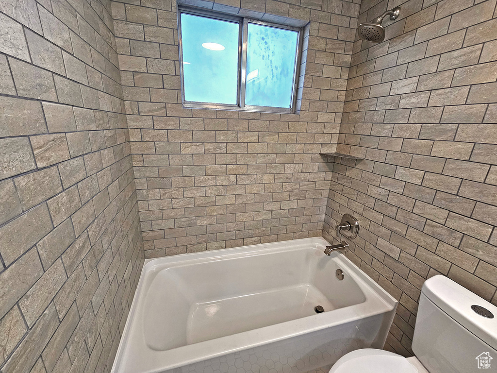 Bathroom featuring tiled shower / bath, toilet, and tile walls