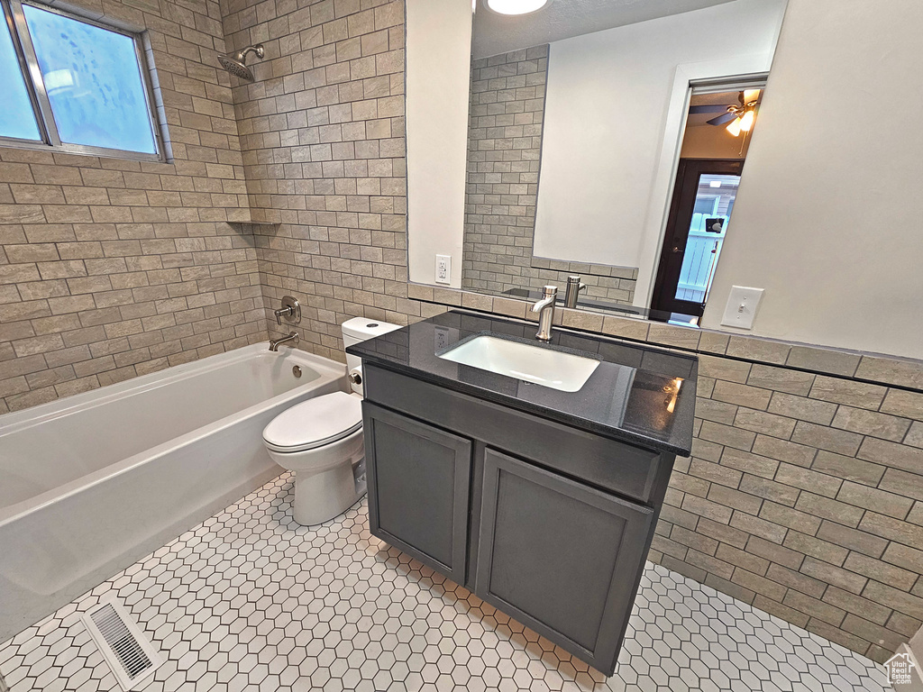 Full bathroom featuring tiled shower / bath, tile walls, vanity, toilet, and tile patterned floors