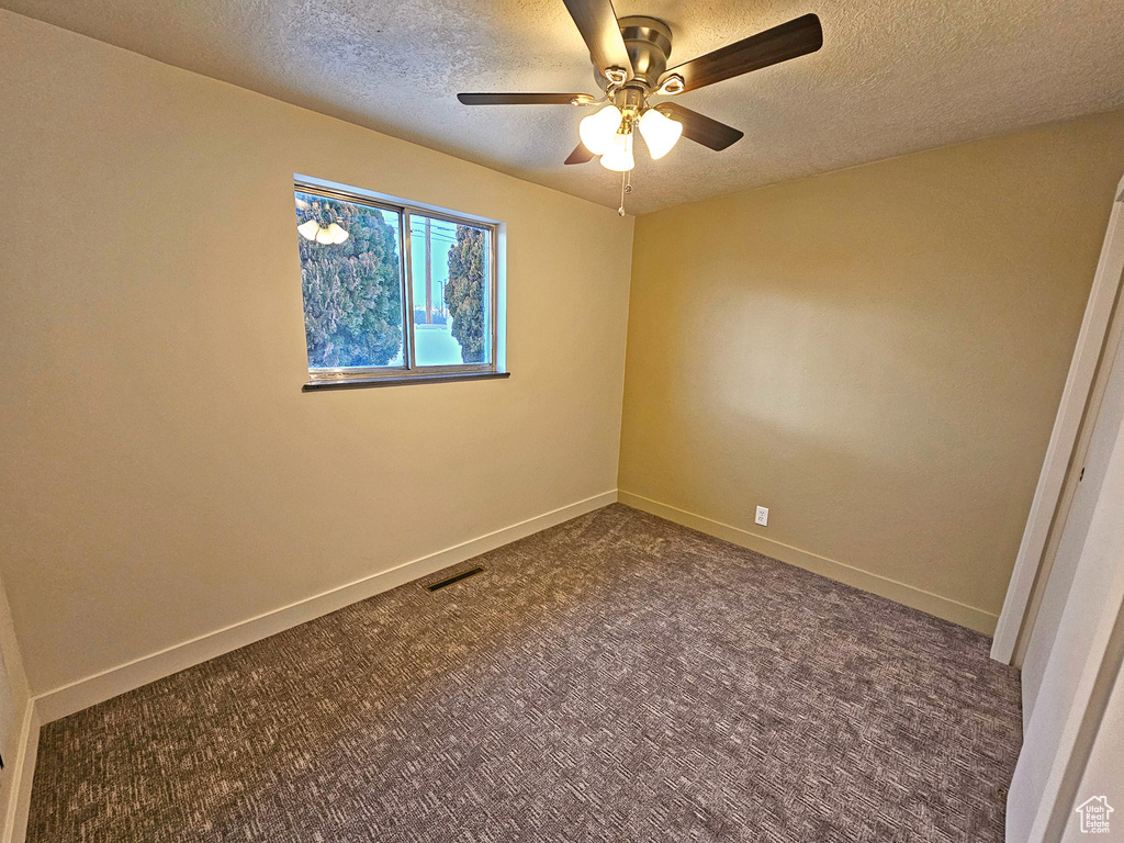 Carpeted empty room with ceiling fan and a textured ceiling