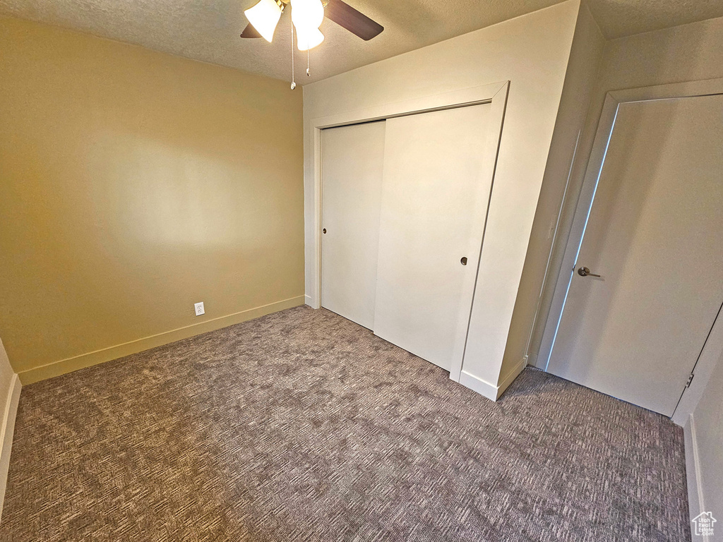 Unfurnished bedroom featuring a textured ceiling, a closet, ceiling fan, and carpet flooring