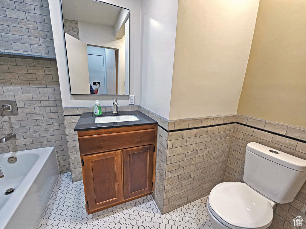 Bathroom featuring toilet, tile walls, vanity, tile patterned flooring, and a washtub