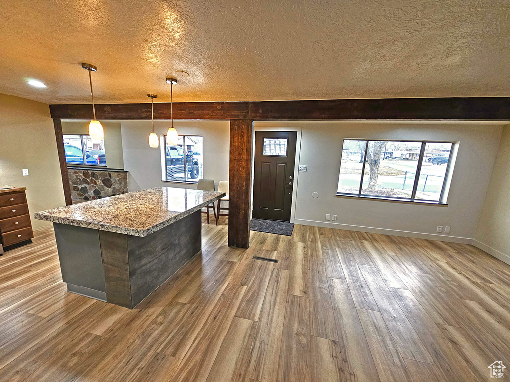 Kitchen featuring pendant lighting, hardwood / wood-style floors, a center island, light stone counters, and a textured ceiling