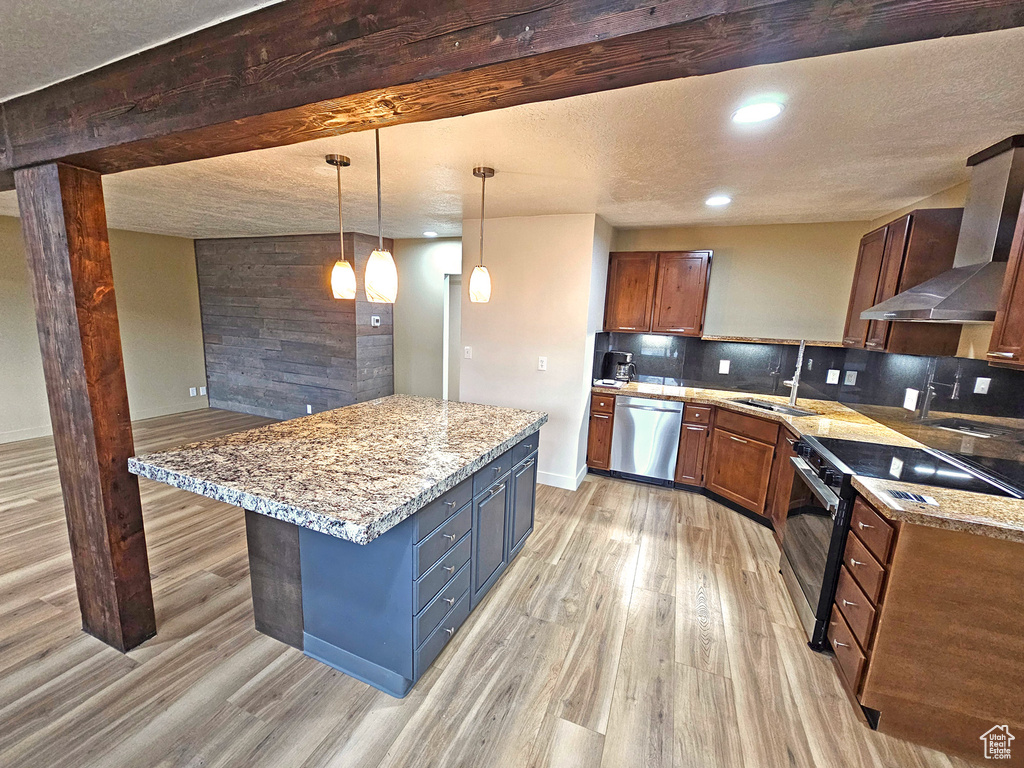 Kitchen with backsplash, hanging light fixtures, light stone counters, stainless steel appliances, and wall chimney exhaust hood