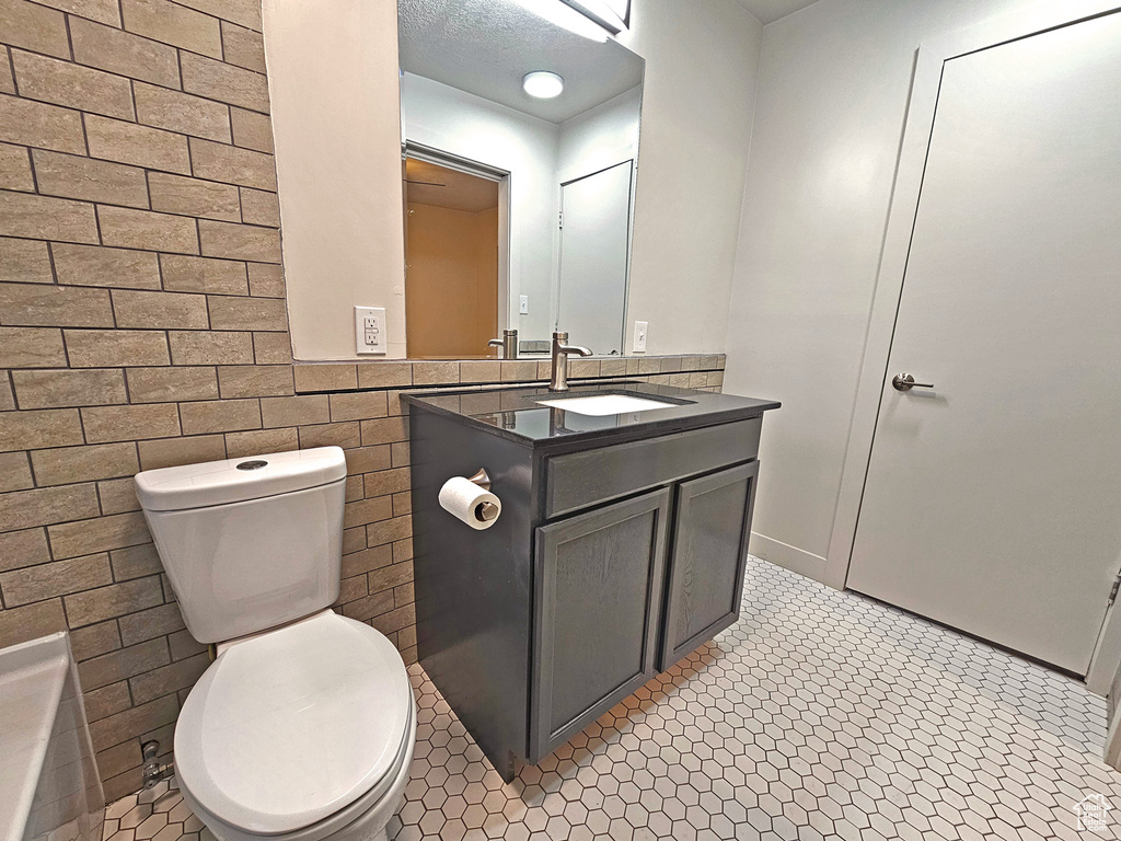 Bathroom with tile walls, vanity, tile patterned flooring, and toilet