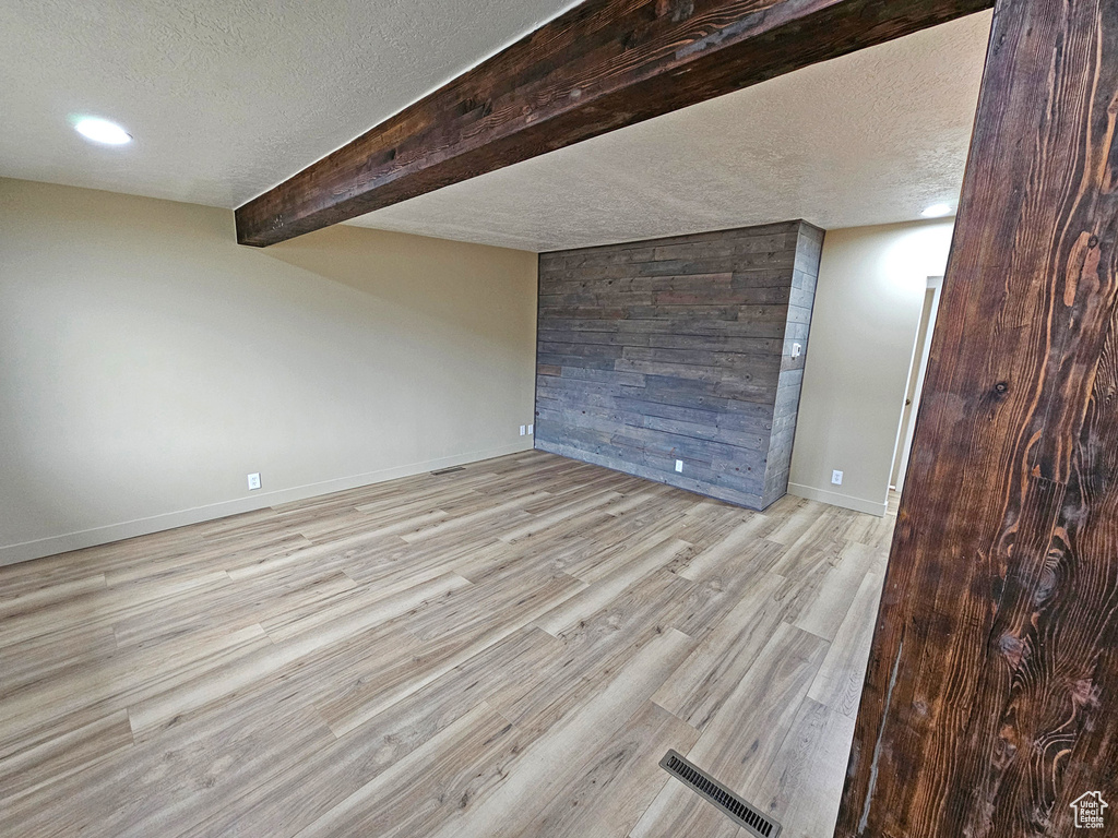 Unfurnished room featuring beam ceiling, a textured ceiling, and light hardwood / wood-style flooring