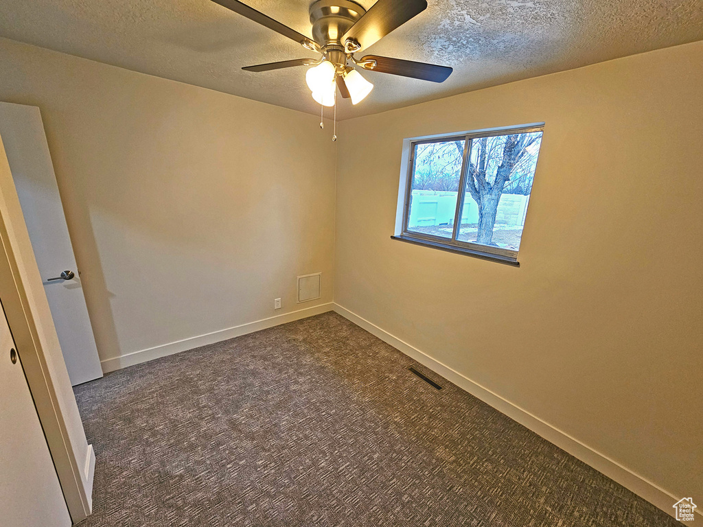 Spare room featuring ceiling fan, dark carpet, and a textured ceiling